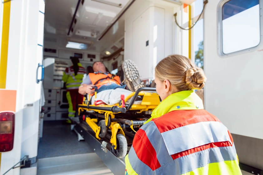 Rettungssanitäterin hebt Patienten auf Krankentrage in den Rettungswagen.